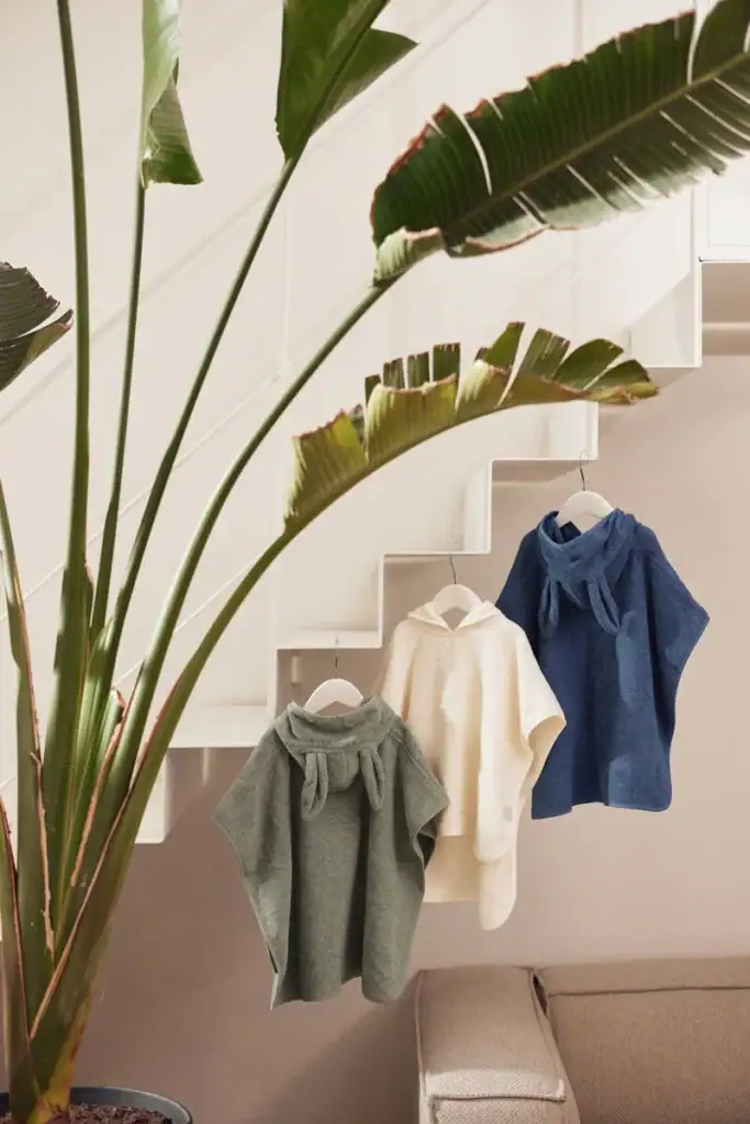 Drie baby badponcho's in grijs, wit en blauw hangen aan een trap.